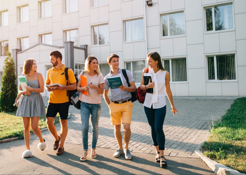 Five friendly students are walking after they passed test outside the college building and discuss the project